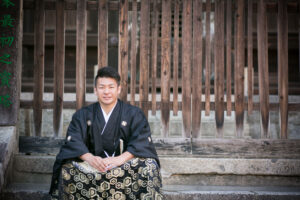 お寺の塀の前に座る袴姿の男性